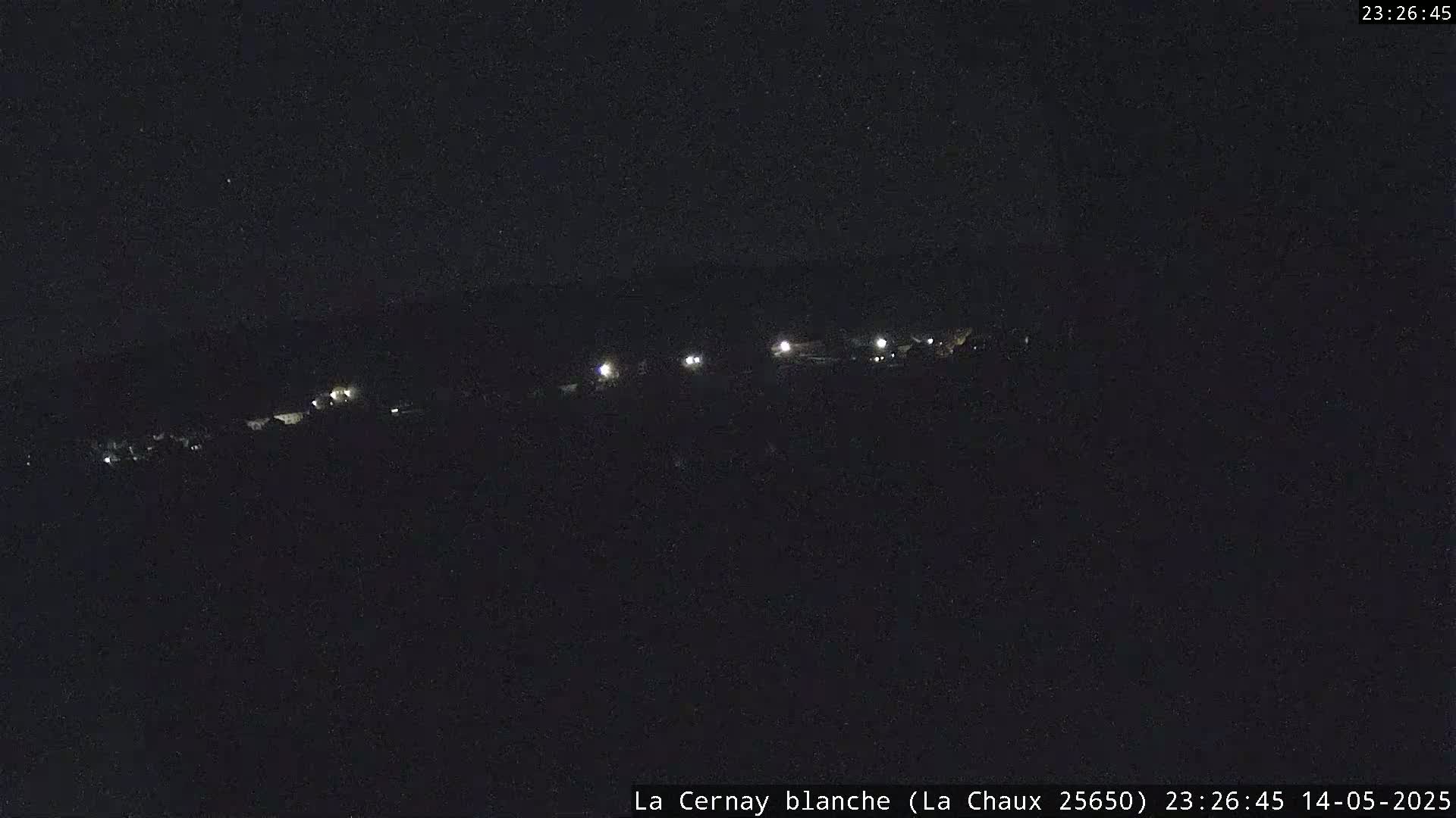 A nighttime long shot shows a dark landscape with a few faint lights visible in the distance under a clear, dark sky.