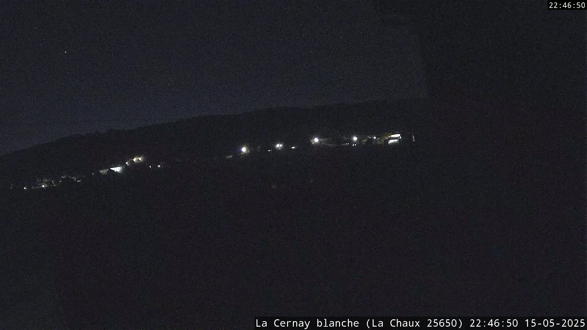 A dark, nighttime view of a distant line of lights in a small settlement under a clear, starless sky.