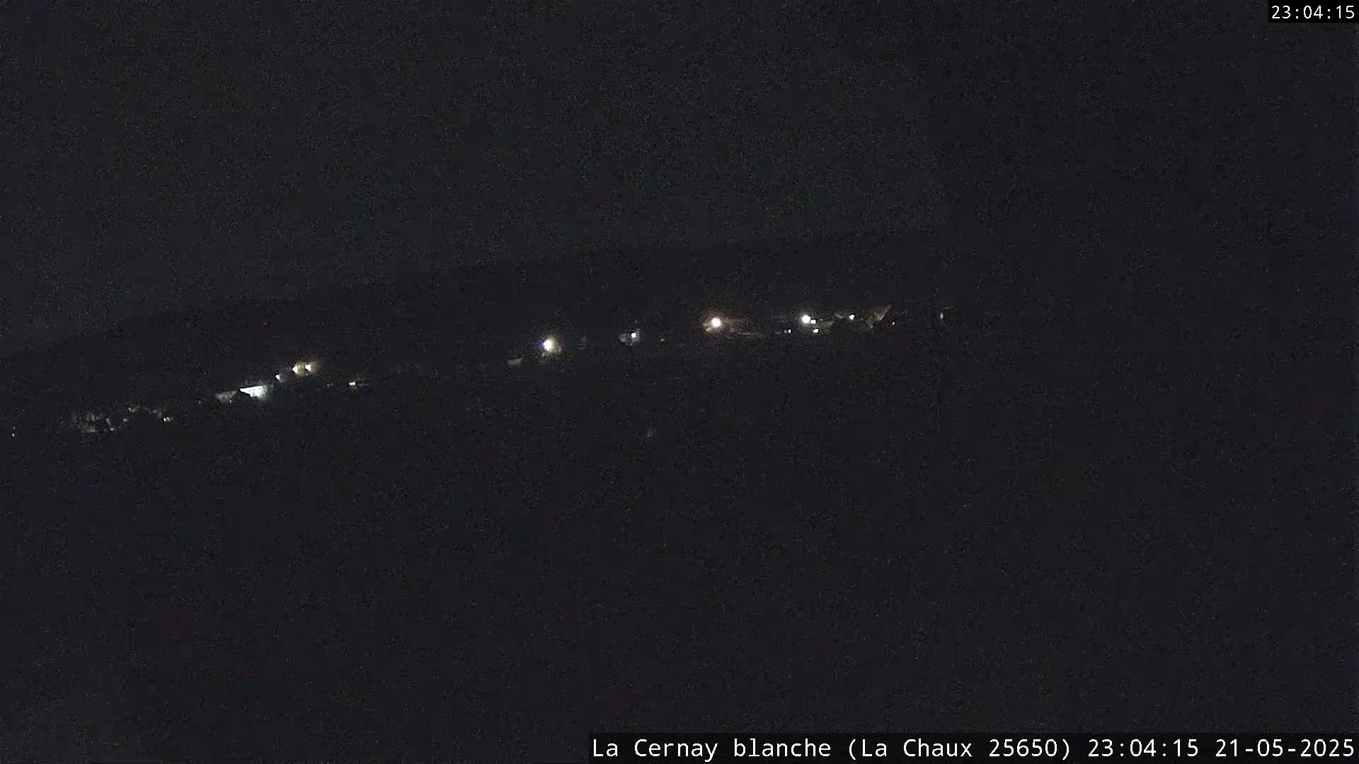 A nighttime, long shot of a dark landscape with a few faint lights visible in the distance.