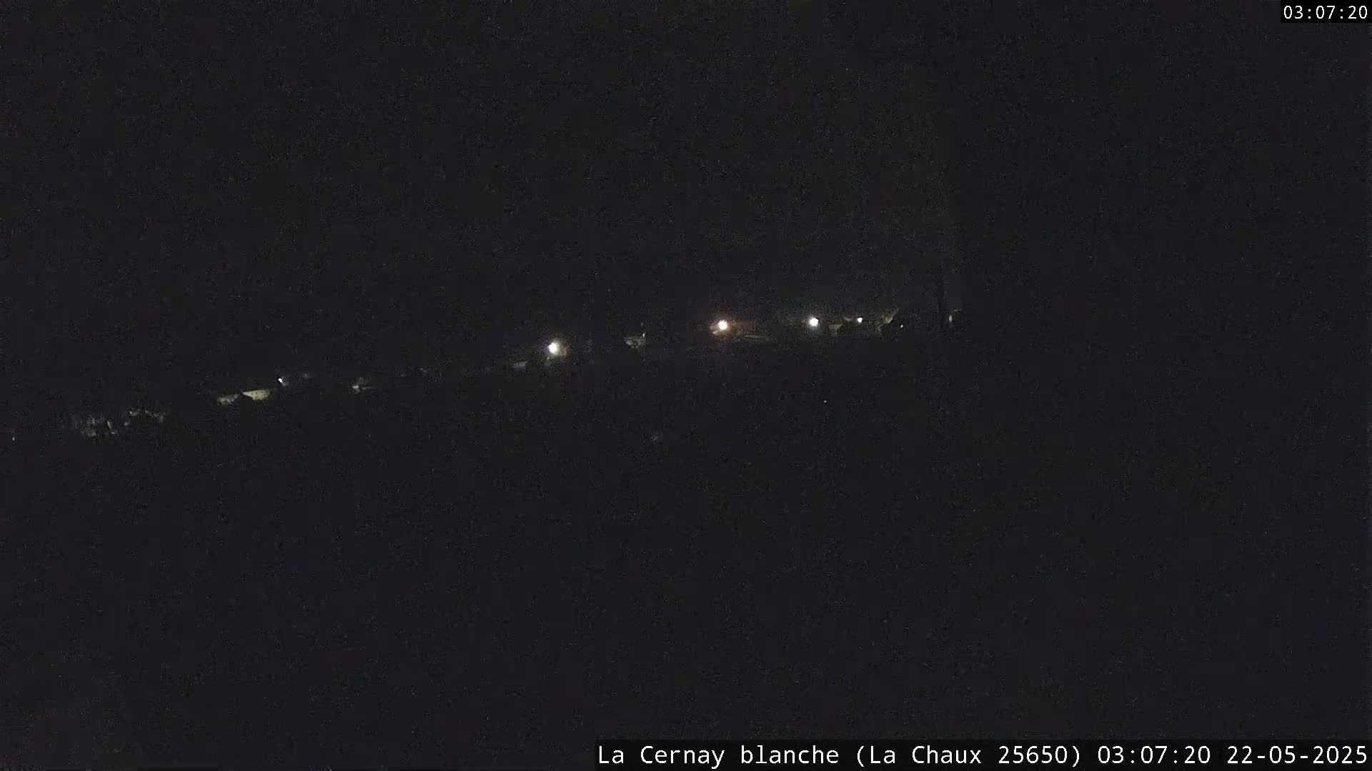 A nighttime, low-light view of a dark landscape with several distant lights visible.