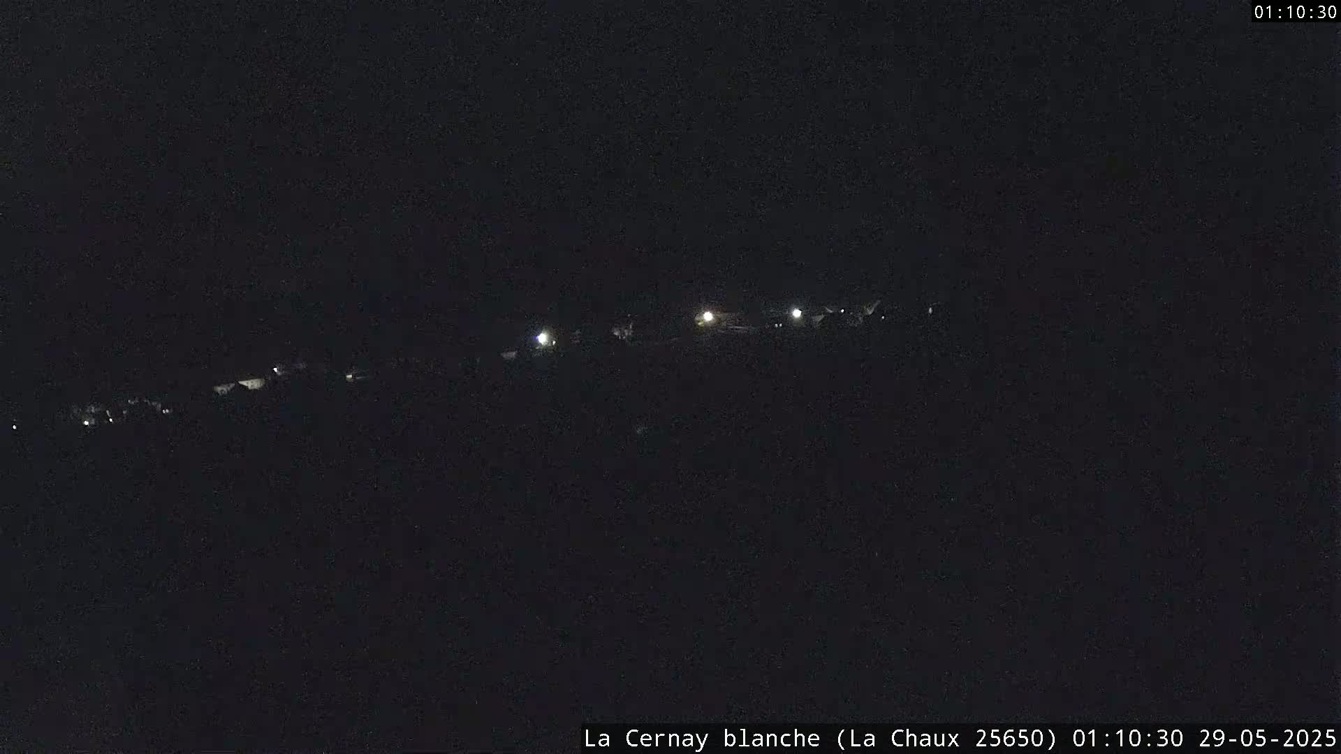 A dark, nighttime landscape shows a line of dimly lit buildings in the distance.