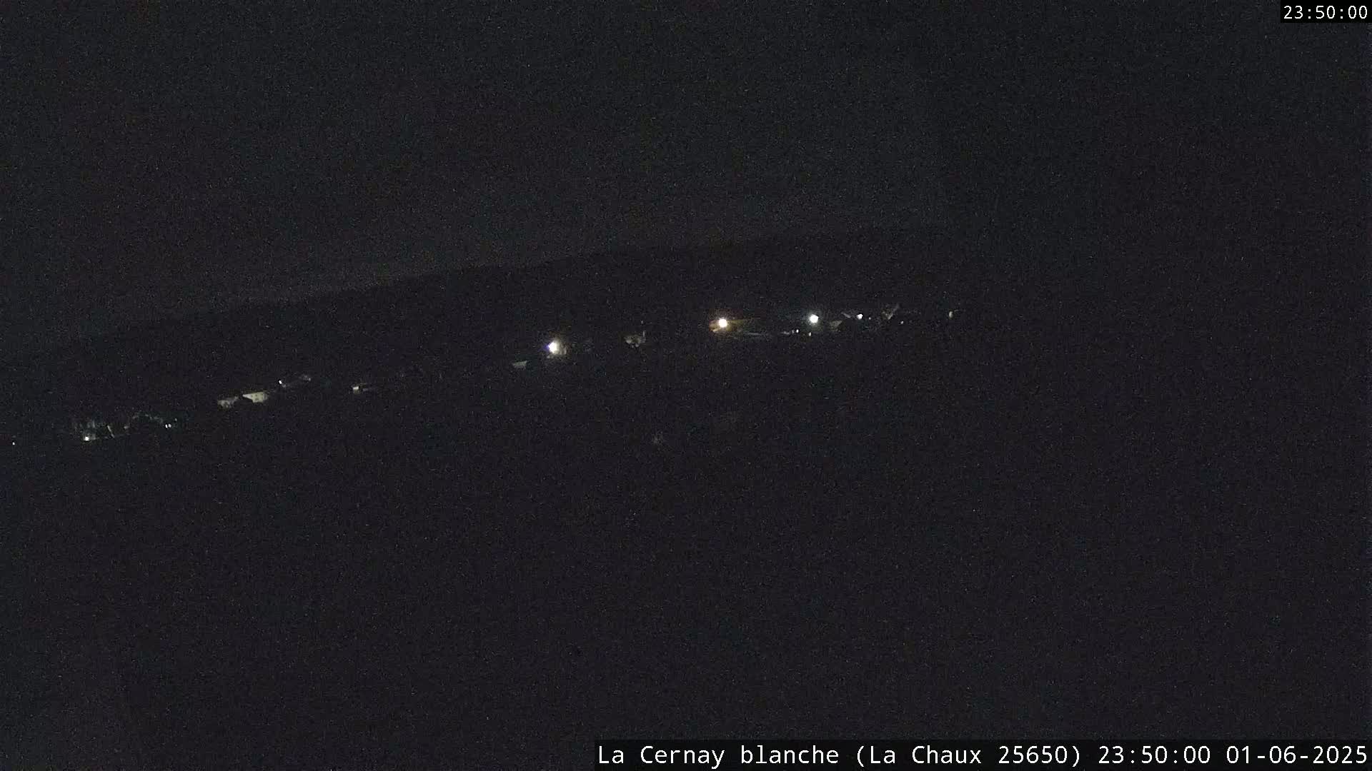 A nighttime, long shot shows a line of faint lights in the distance across a dark landscape under a clear, dark sky.