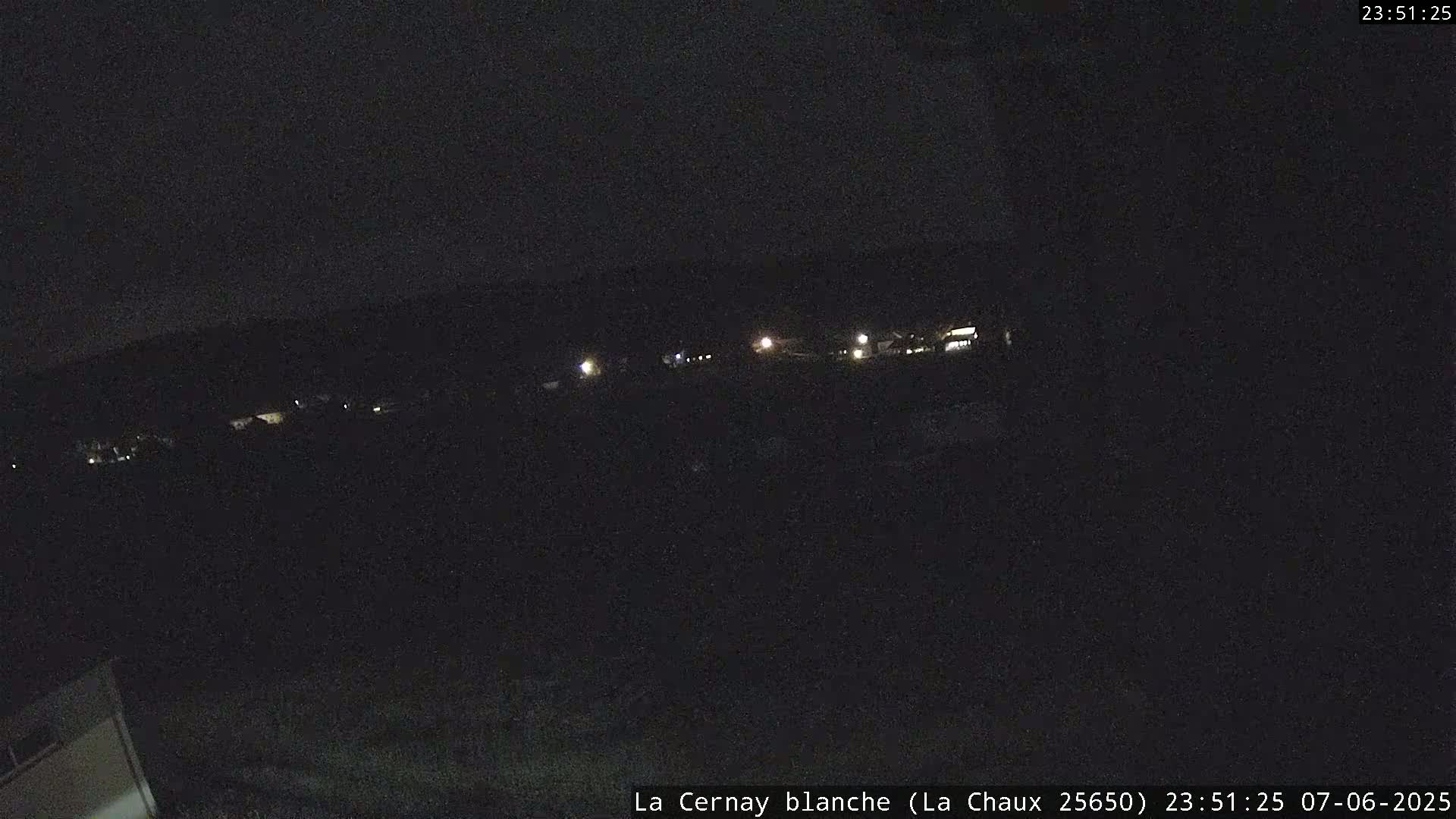 A nighttime, long-range view shows a dark landscape with a few distant lights.