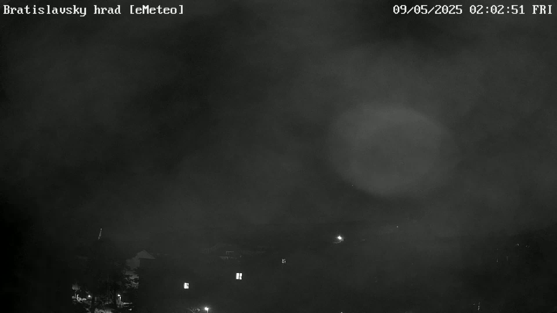 A nighttime, hazy view shows a dark sky and dimly lit buildings in the distance.