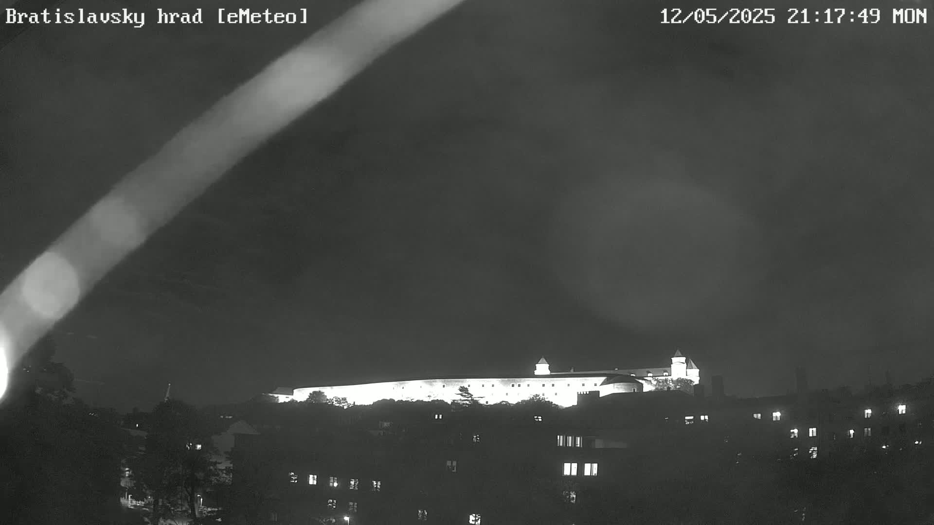 A brightly lit castle sits atop a hill at night under a dark, cloudy sky.