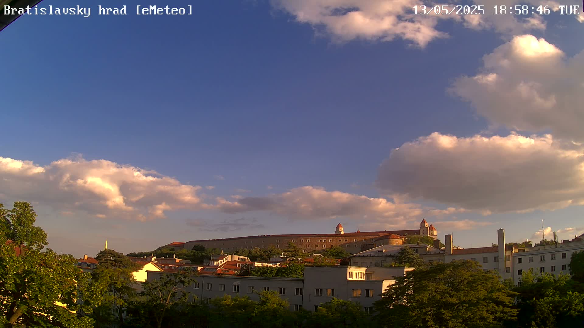 A partly cloudy sky over a city with a large castle-like structure on a hill in the background.