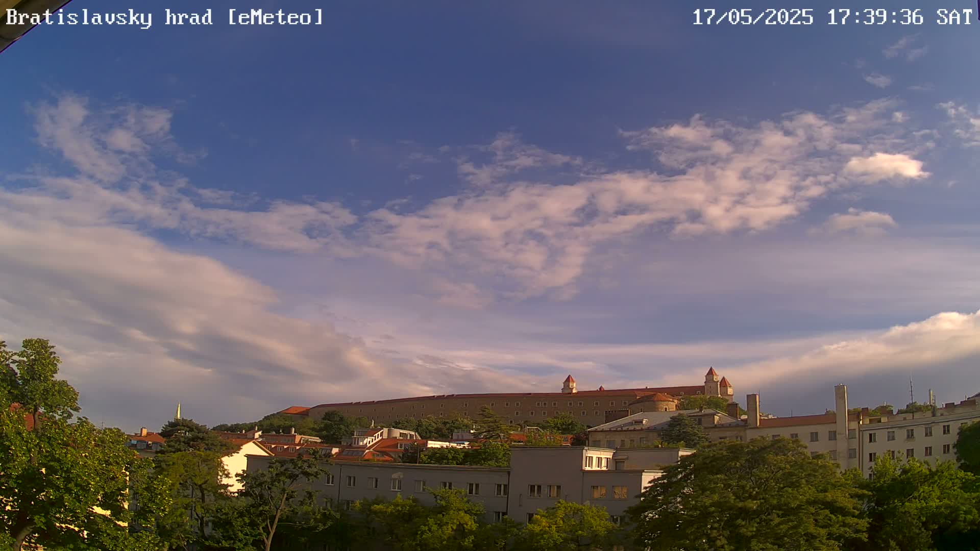 A large castle sits atop a hill overlooking a city under a partly cloudy sky.