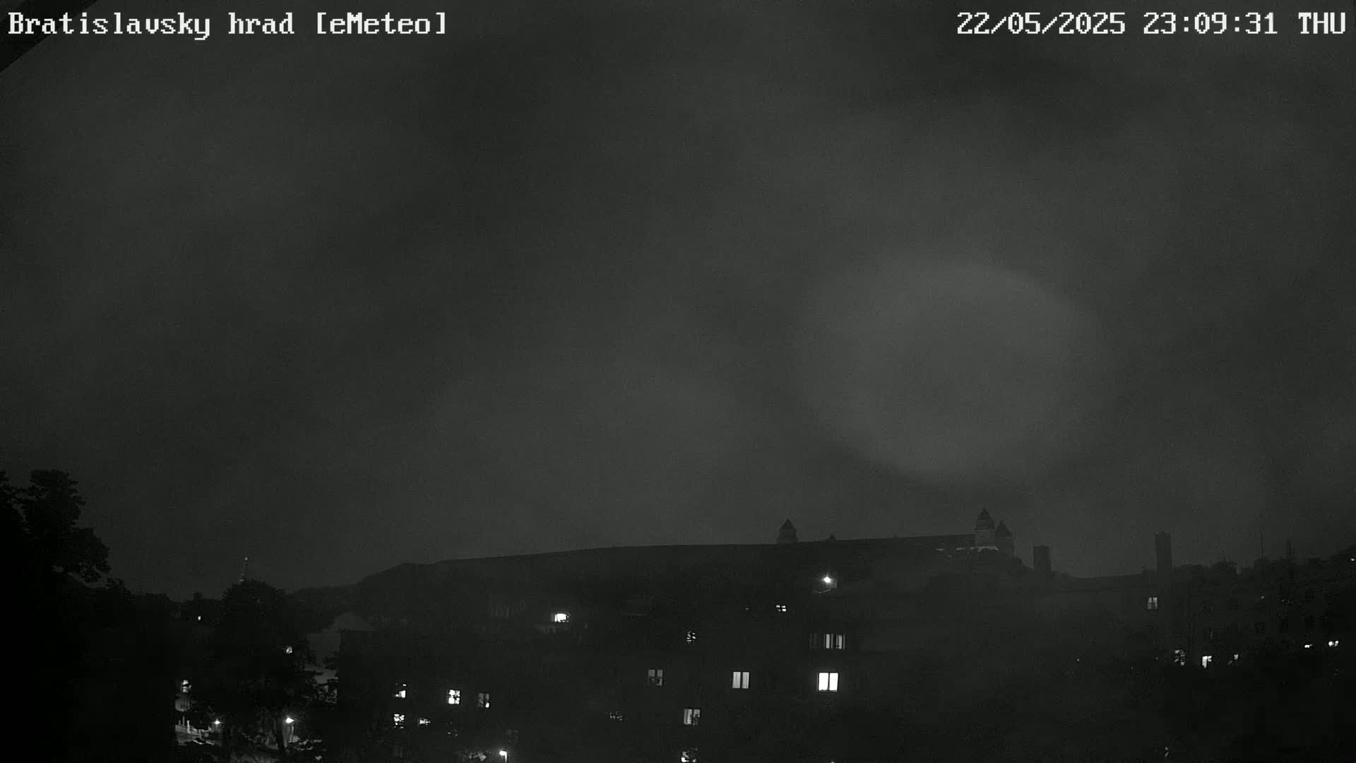 A nighttime view of a castle-like structure and buildings under a dark, overcast sky.