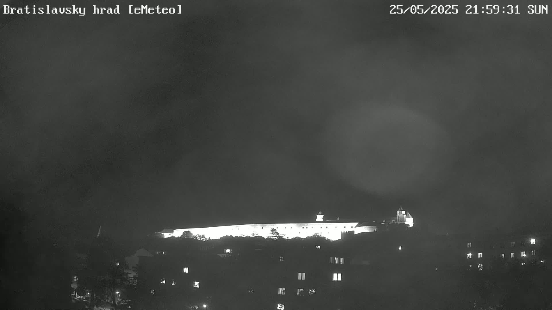 A brightly lit castle sits atop a hill at night under a hazy, dark sky.