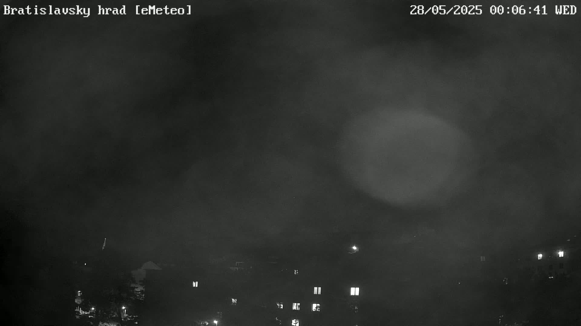 A nighttime, foggy view shows dimly lit buildings below a dark, hazy sky.