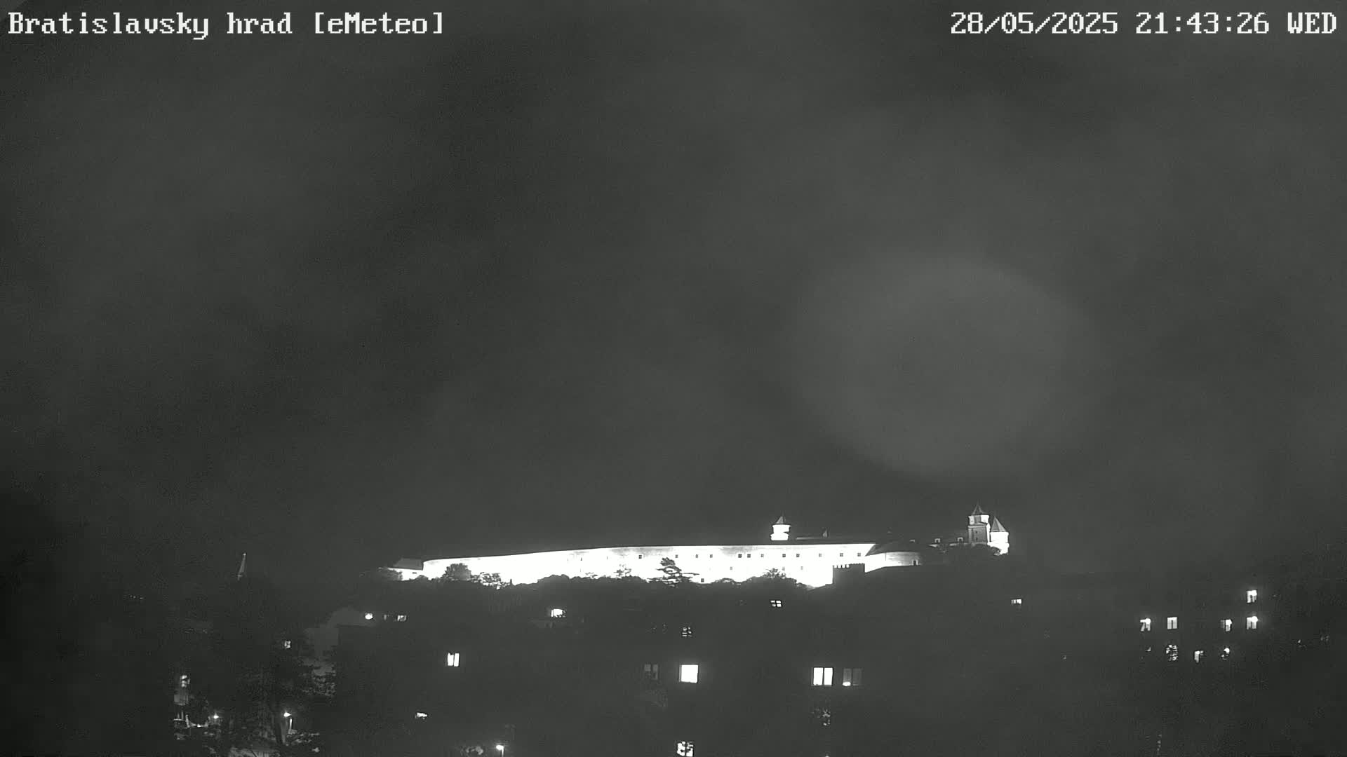 A brightly lit castle sits atop a hill at night under a dark, cloudy sky.