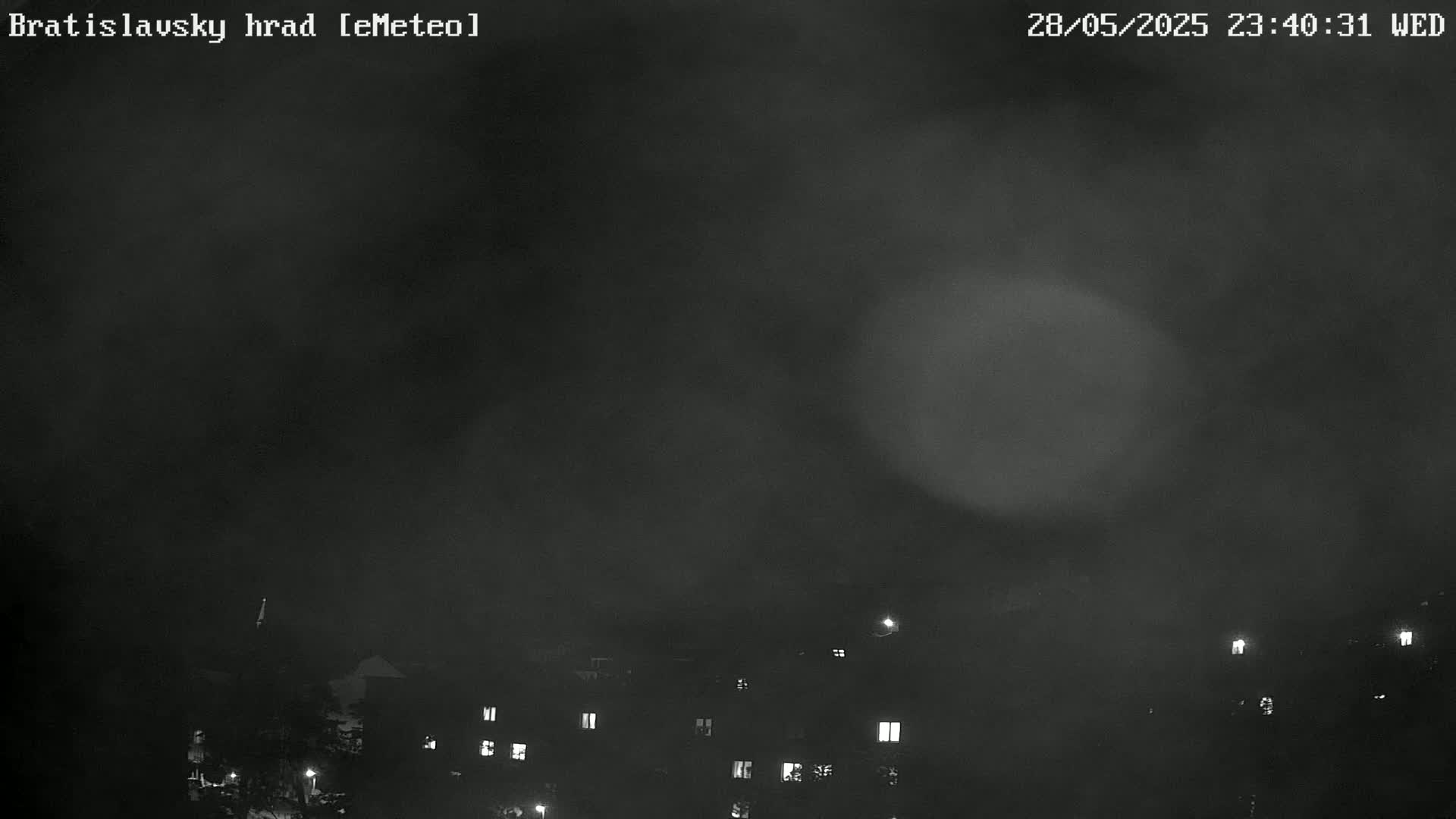 A nighttime, hazy view shows dimly lit buildings below a dark sky.