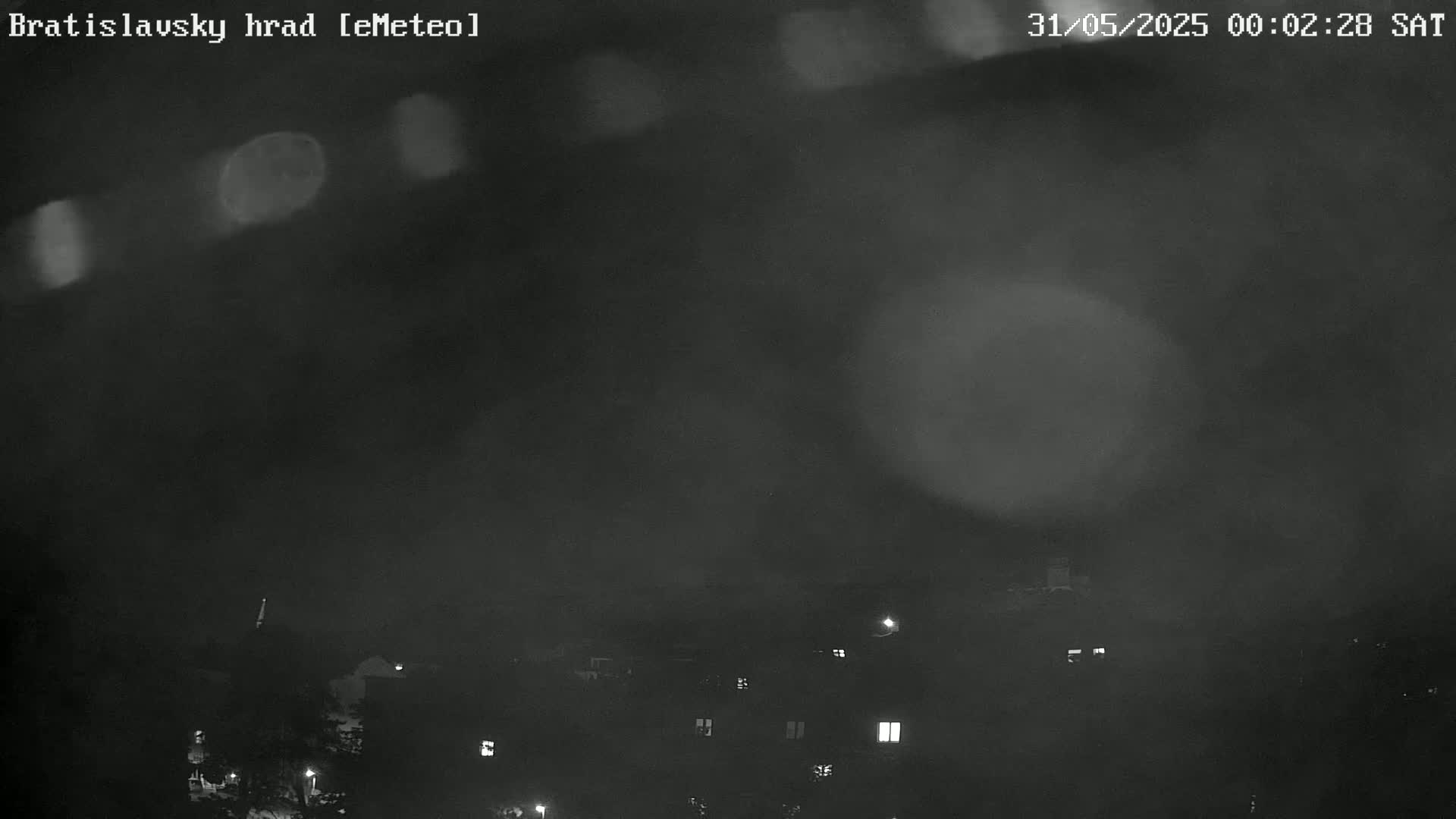 A nighttime, blurry view of a town or city obscured by fog or mist, with a few lights visible in the distance.