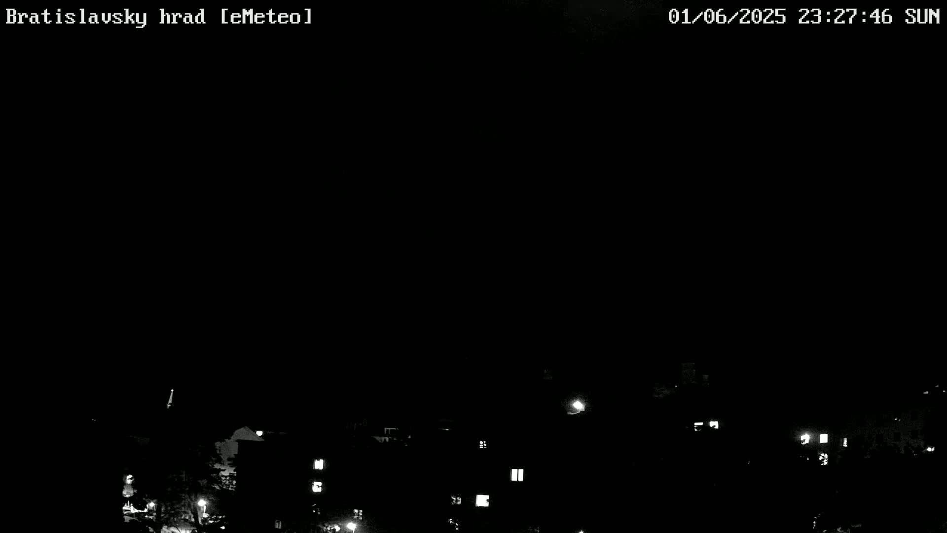 A nighttime, dark, mostly clear view of a cityscape with dimly lit buildings and trees.