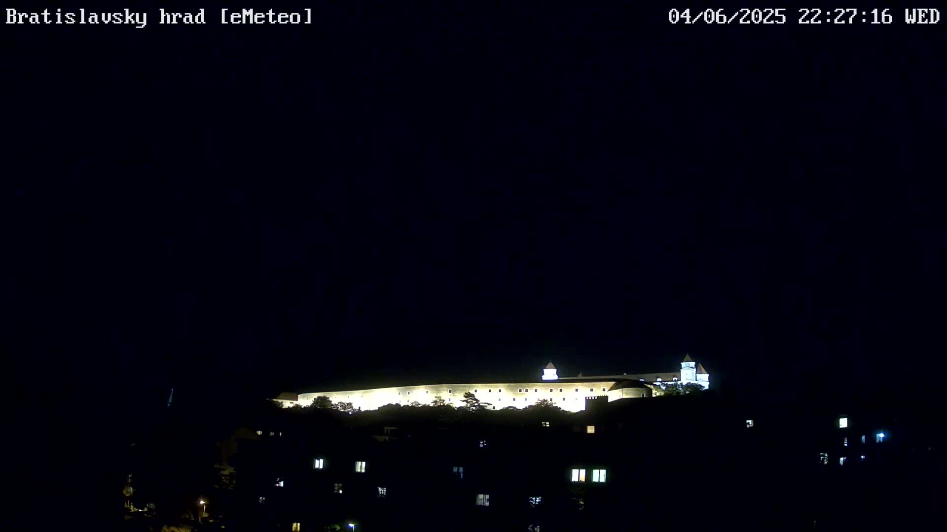 A brightly lit castle sits atop a hill at night under a clear, dark sky.