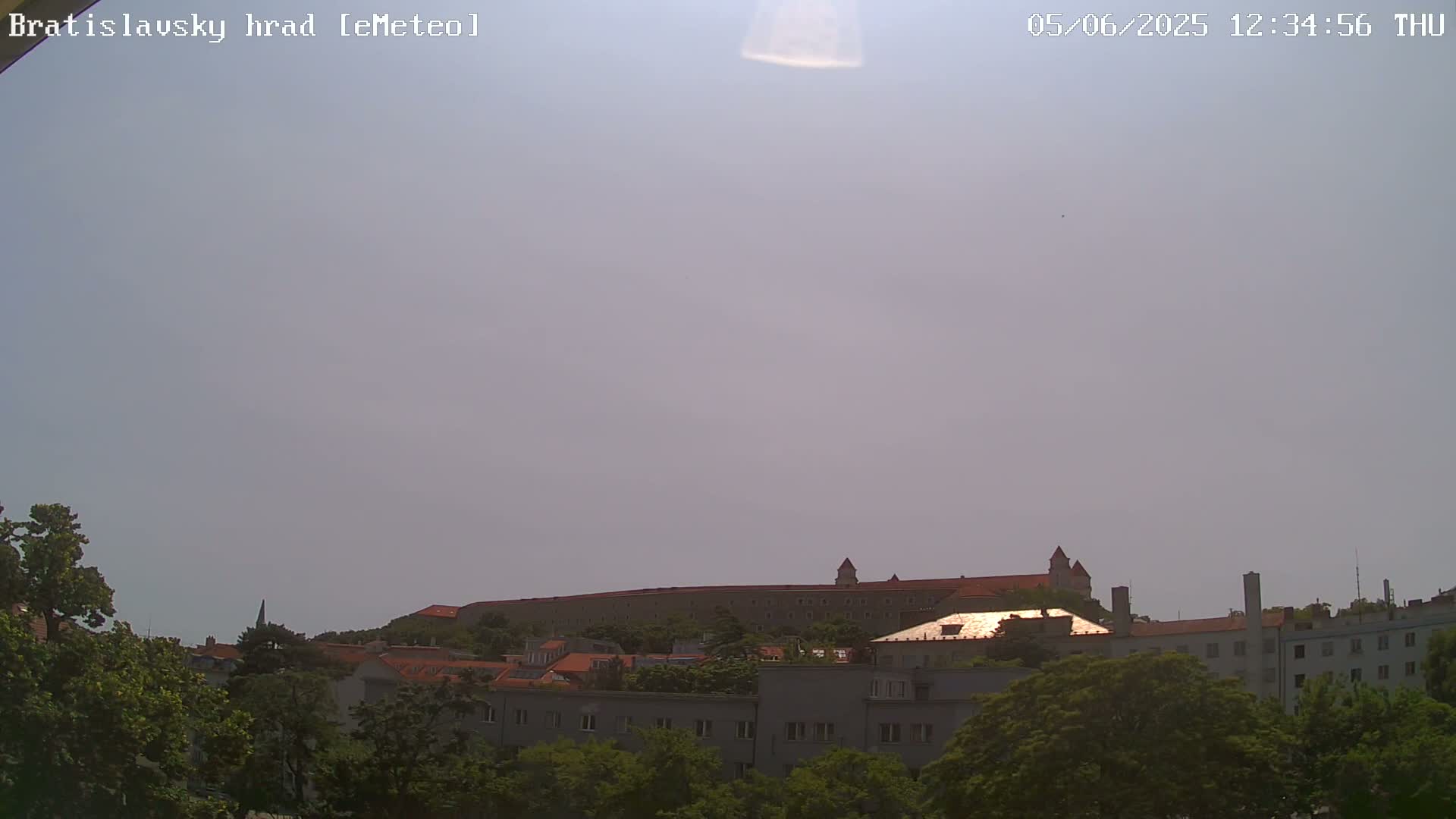 A large castle sits atop a hill overlooking a town, under a hazy, light-grey sky.