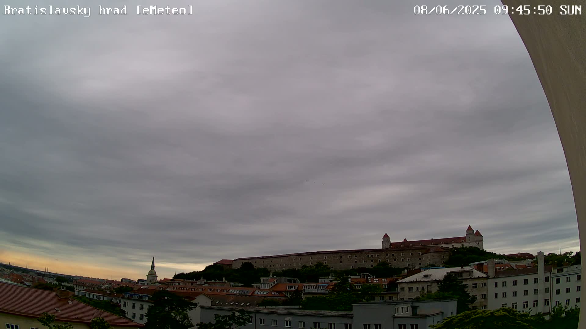 A large stone castle sits atop a hill overlooking a city under a mostly cloudy sky.