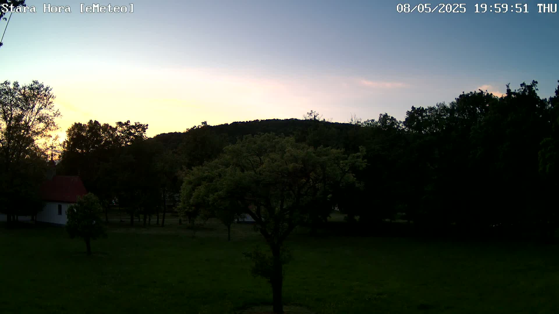 A grassy field with trees and a small building is visible at dusk under a mostly clear sky.