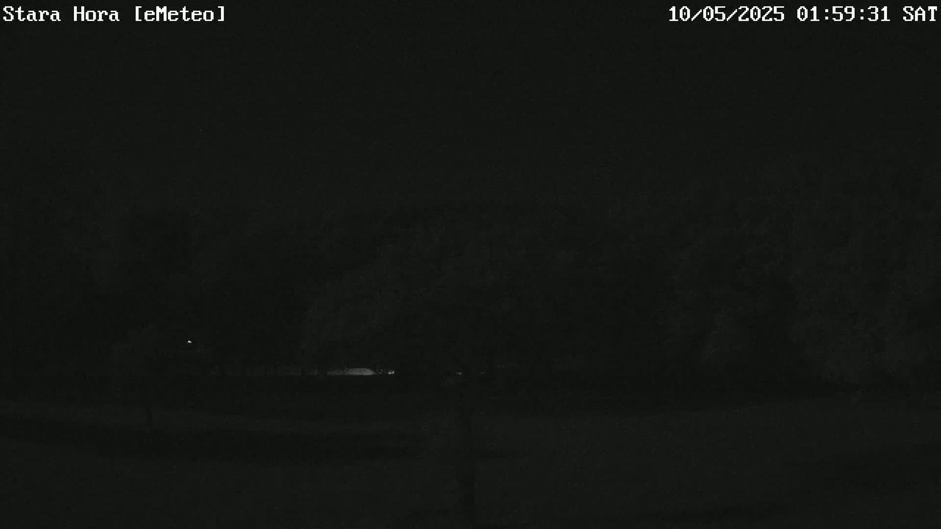 A dark nighttime scene shows a mostly obscured landscape with a few faint lights visible in the distance.