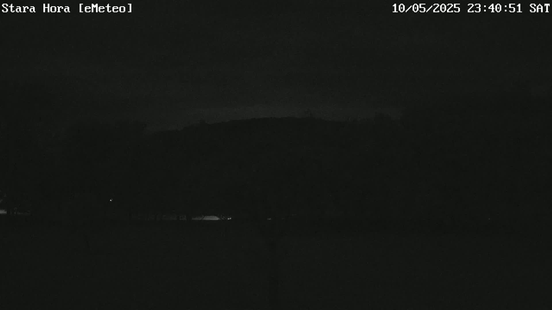 A dark nighttime scene shows a hill silhouetted against a mostly clear, dark sky.