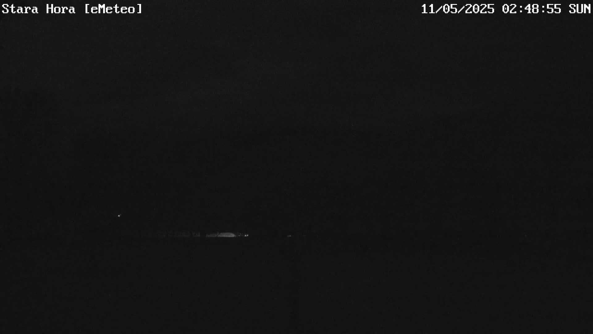 A nighttime, low-light view shows a dark landscape with a few faint lights visible in the distance.