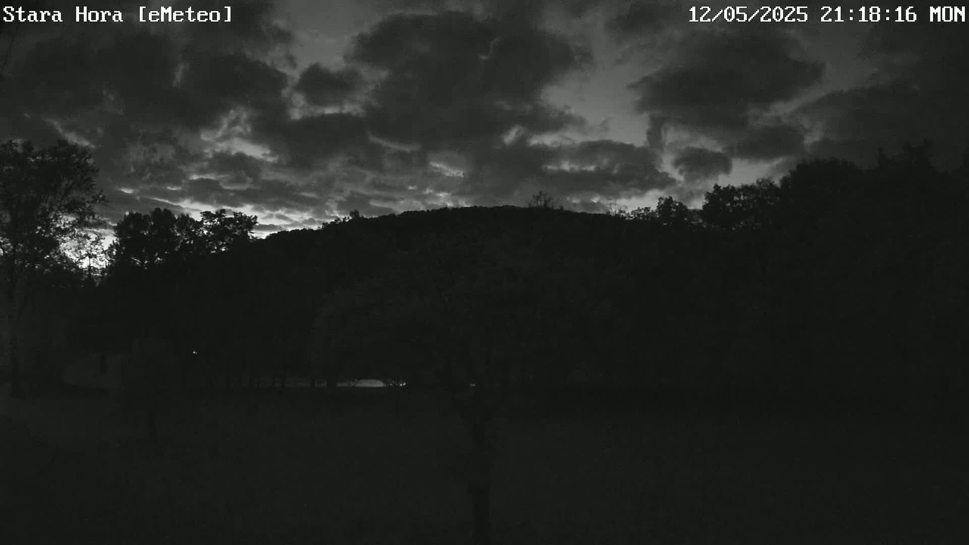 A dark, overcast sky over a silhouetted landscape of trees and a hill at twilight.