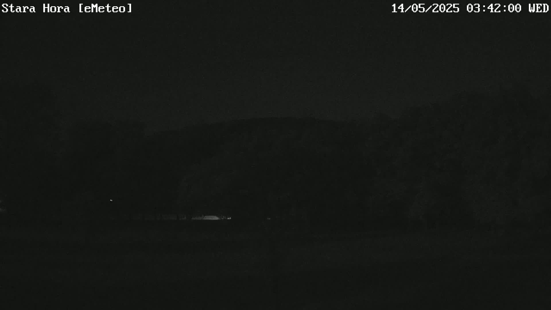 A dark nighttime scene shows a flat expanse of land leading to a dark, silhouetted hill under a clear, dark sky.