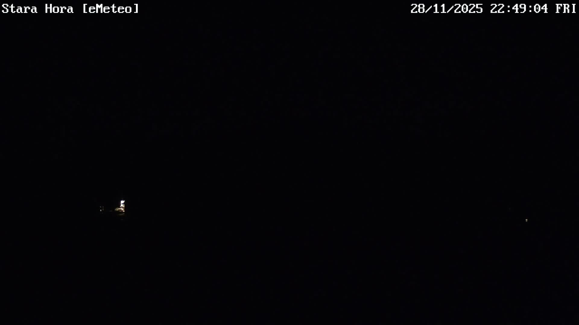 The image shows a very dark outdoor scene at night with a few distant, faint lights visible on the horizon under clear skies.