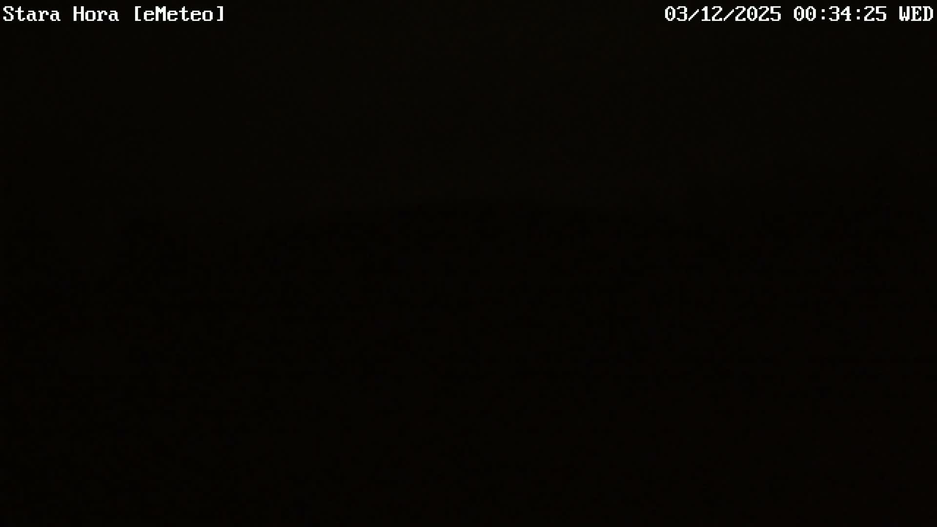 An extremely dark outdoor night scene shows only faint, indistinct shapes against a black background, indicating clear but unlit conditions.