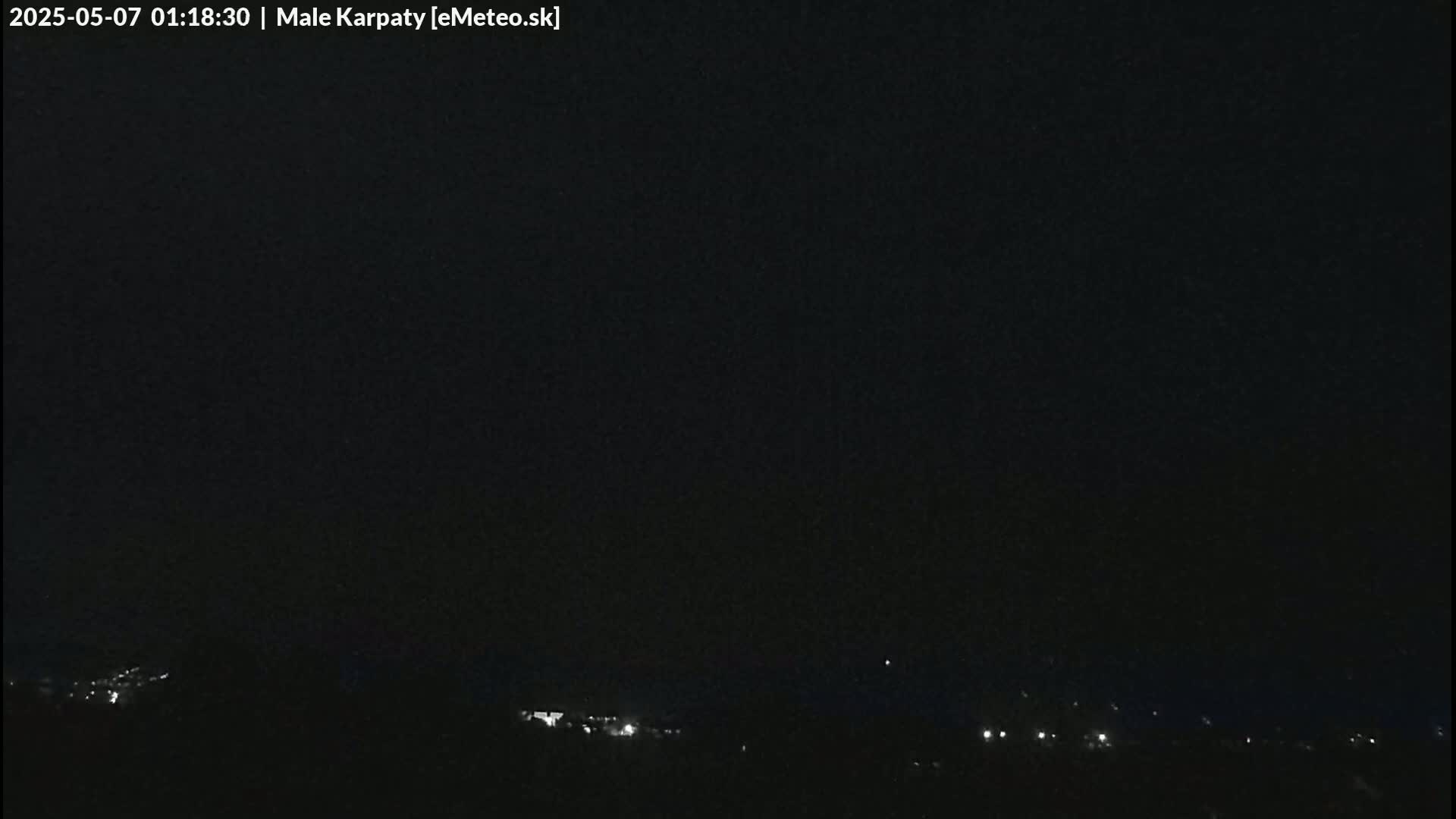 A dark nighttime scene shows a distant line of faint lights at the bottom of the frame, under a completely clear, black sky.