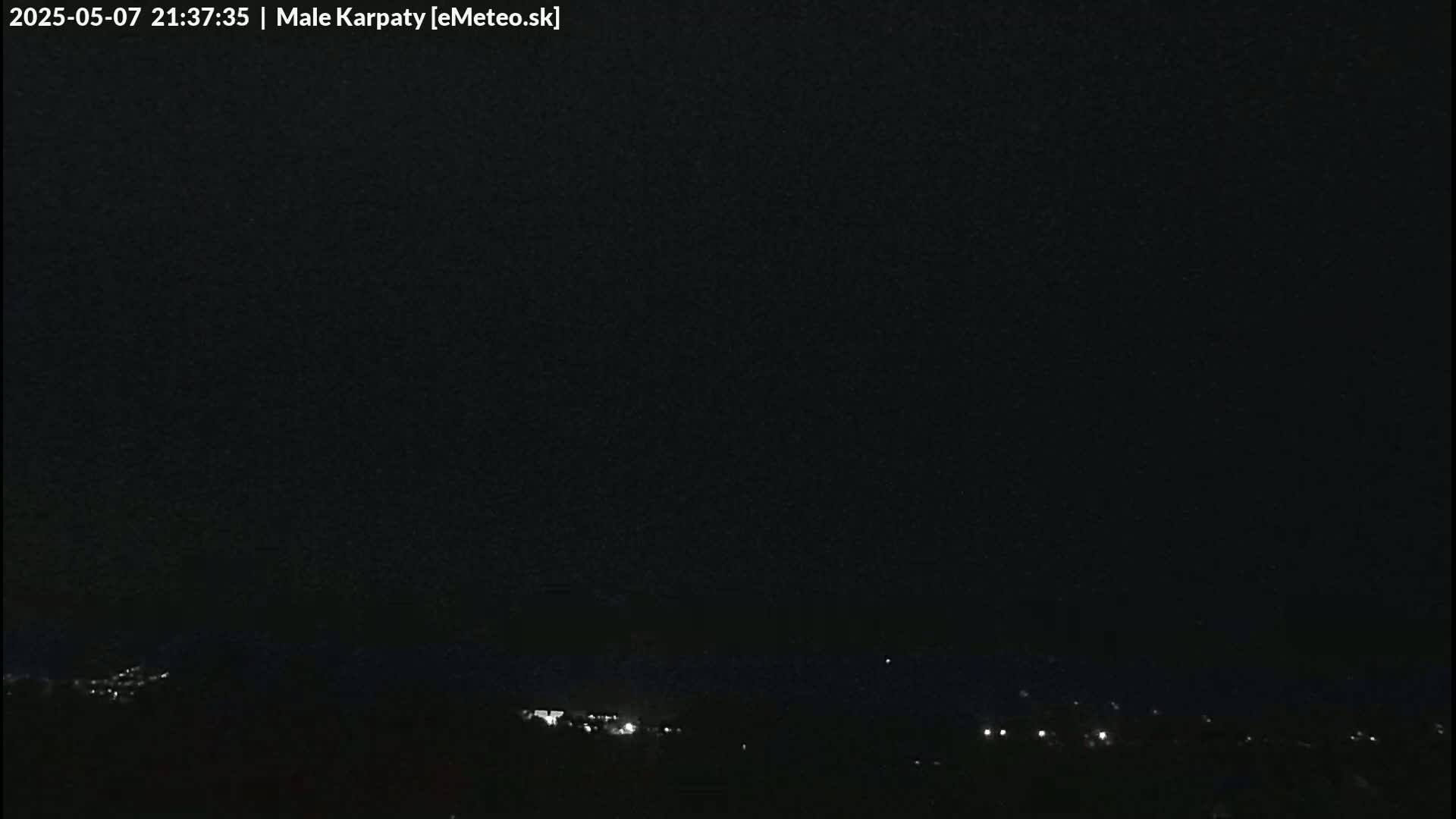 A nighttime view shows dimly lit buildings and hills under a dark, clear sky.