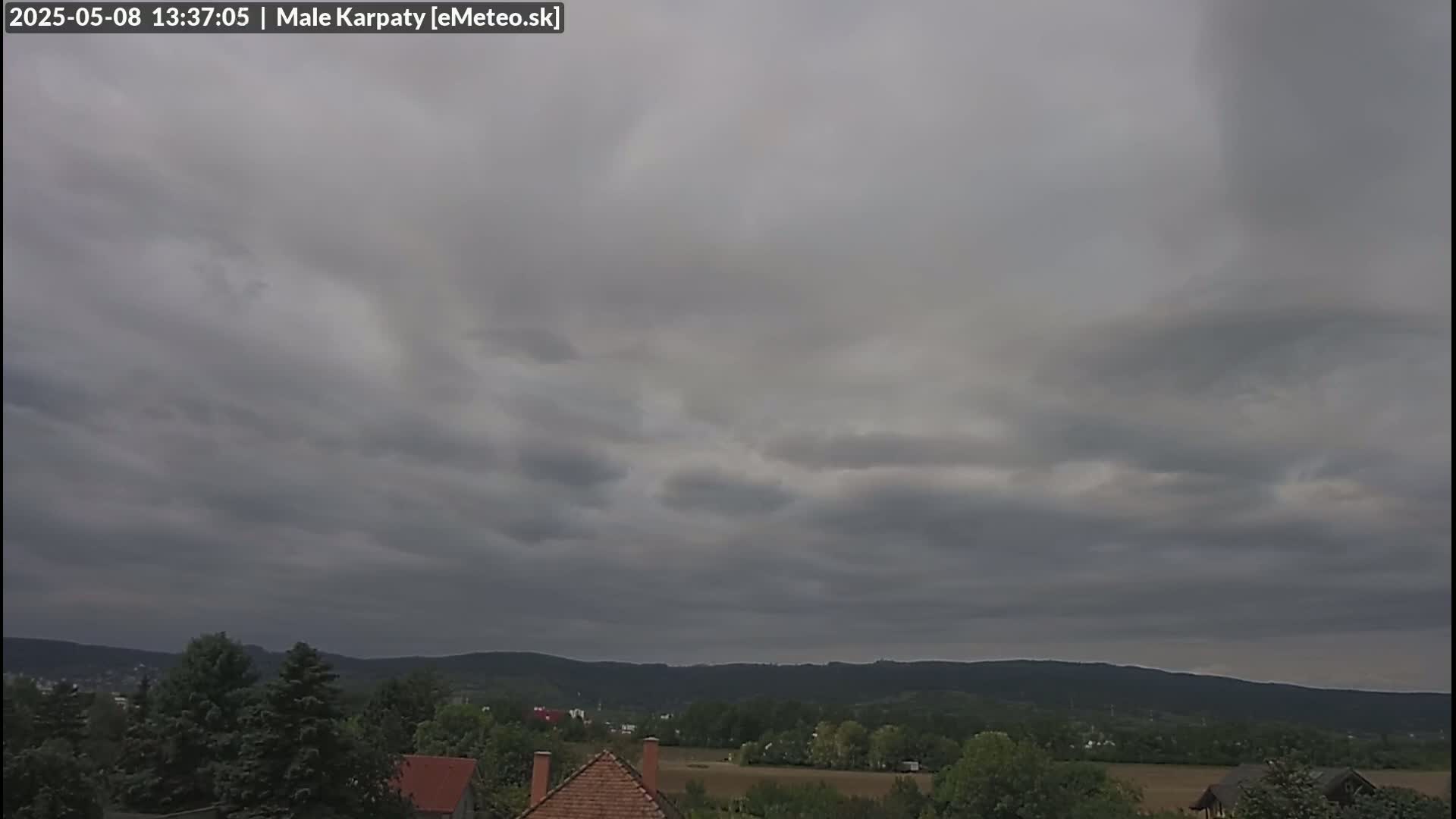 Overcast skies hang above a landscape of low hills, trees, and a few houses.