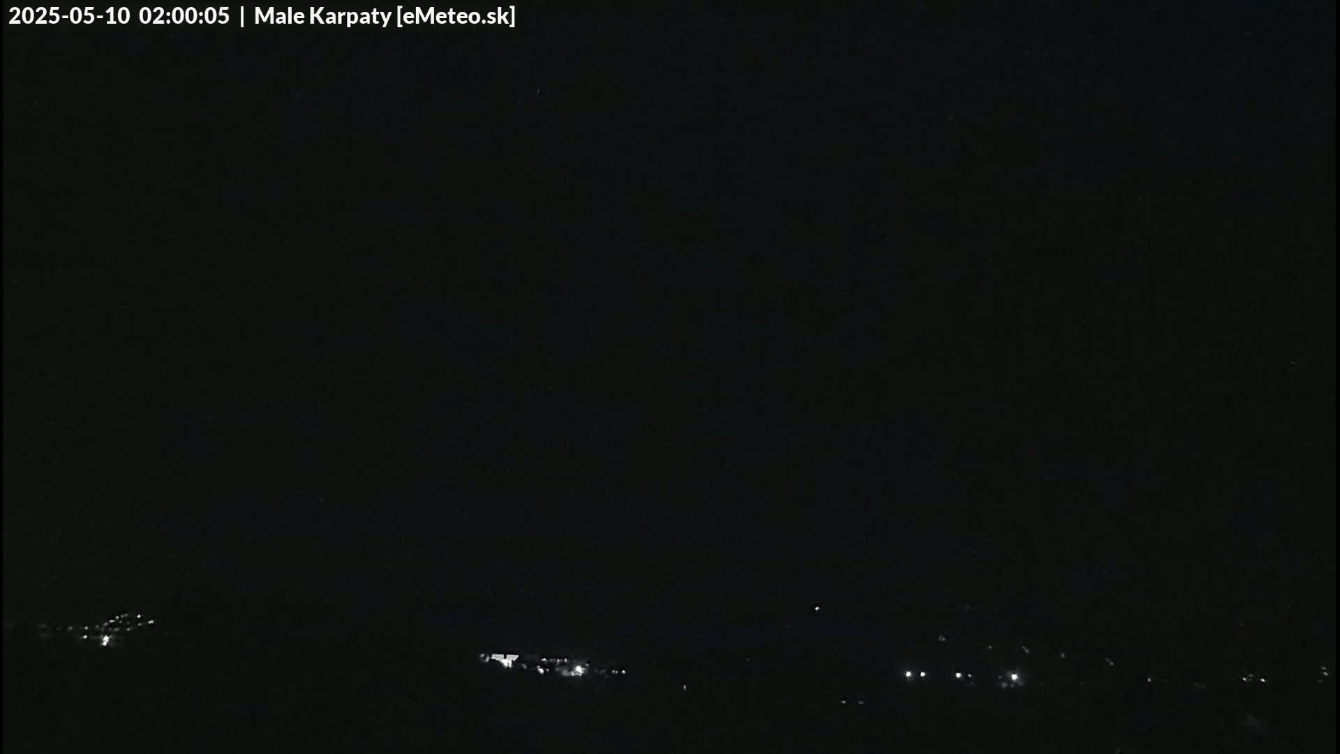 A dark nighttime scene shows a few faint lights in the distance under a clear, black sky.