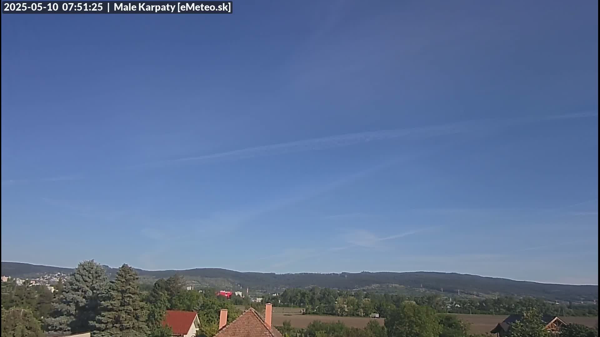 Under a clear blue sky, a view shows a hilly landscape with green trees and houses,  in the distance.