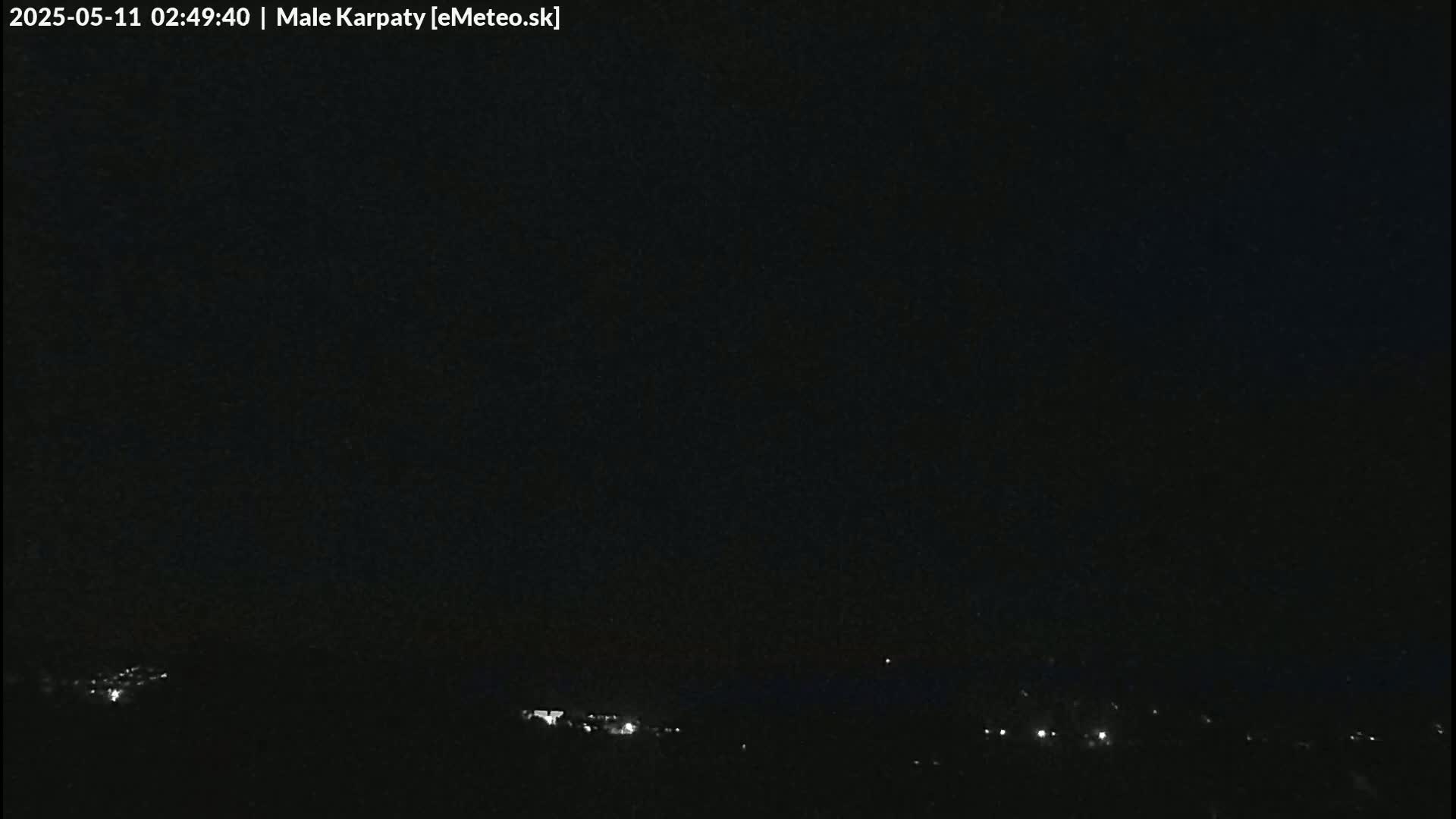 A nighttime, dark view of a landscape with a few faint lights visible in the distance under a clear, black sky.