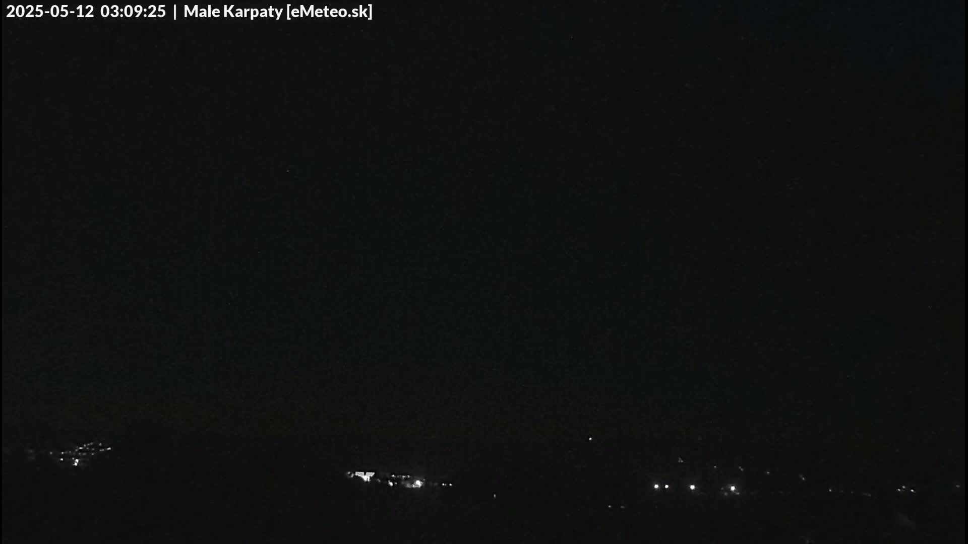 A dark nighttime scene shows a distant line of faint lights at the bottom of the frame against a completely black sky.