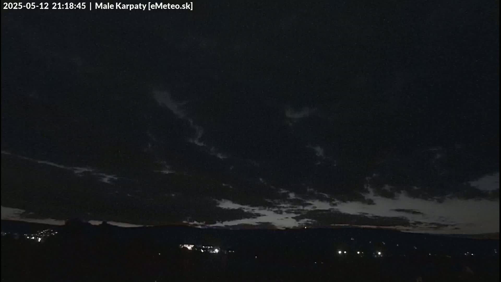 A nighttime landscape shows a dark sky with thin clouds and a few distant lights on a horizon.
