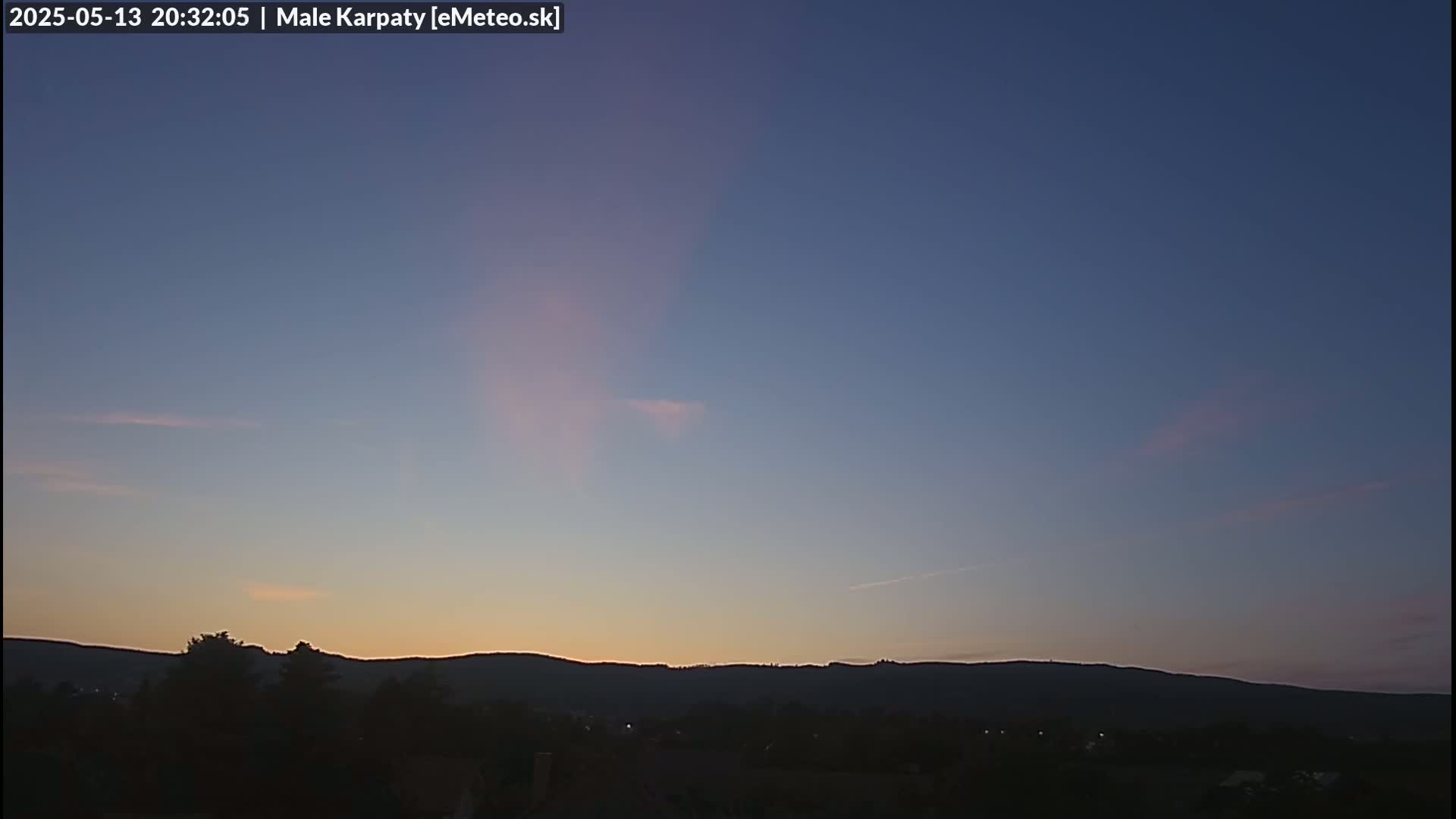 A mostly clear twilight sky with faint pink hues near the horizon above a dark silhouette of distant hills and trees.