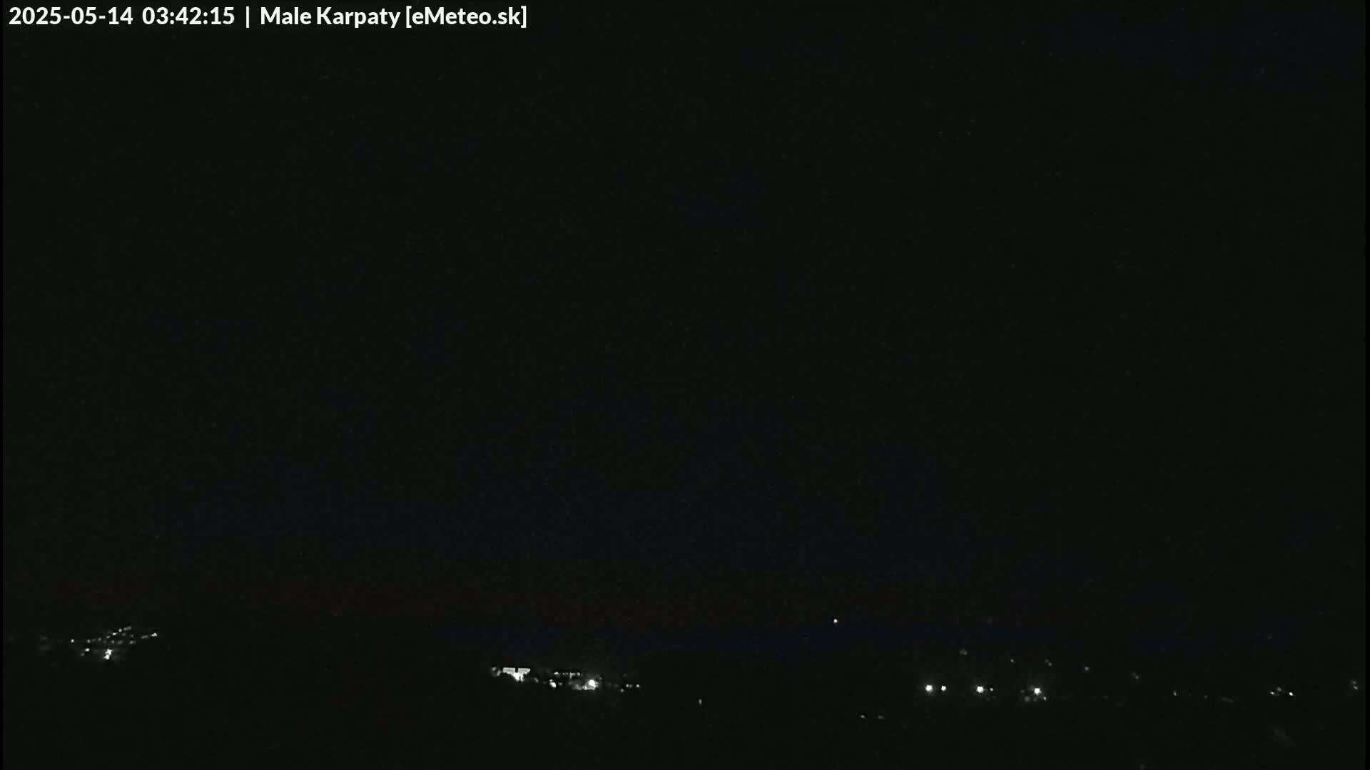 A dark nighttime scene shows a distant line of faint lights, likely from a town or village, under a clear, black sky.