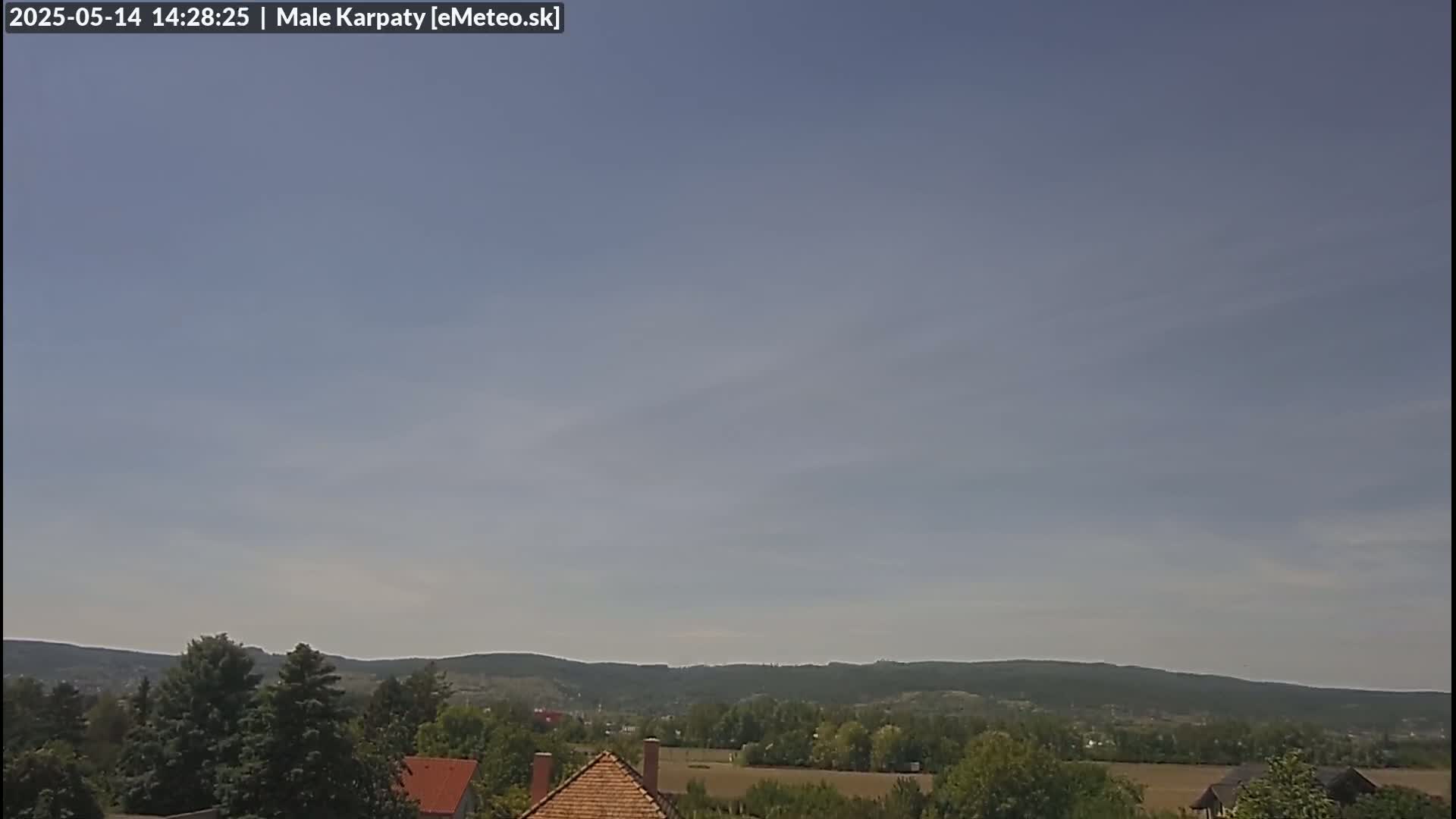 A mostly clear sky overlooks a landscape of green hills, trees, and a few buildings.