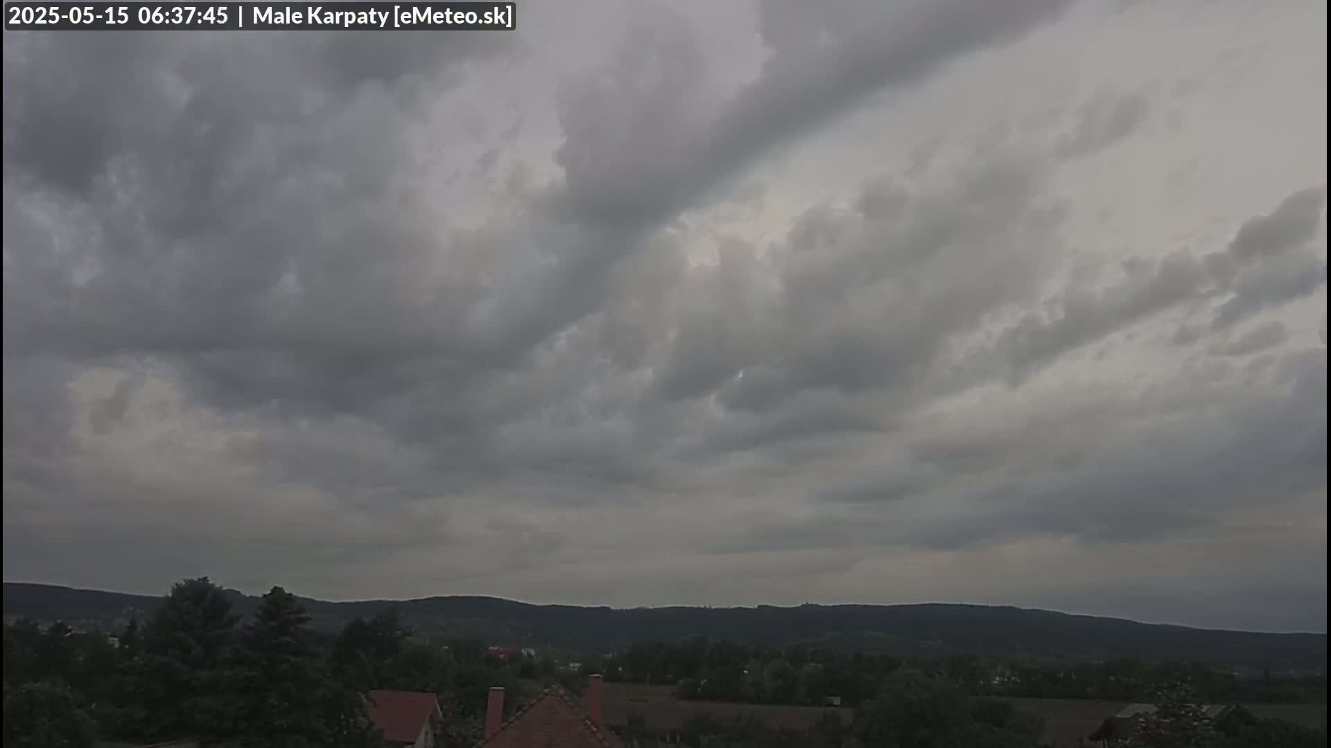 Overcast skies loom over a landscape of dark green hills and a small village.