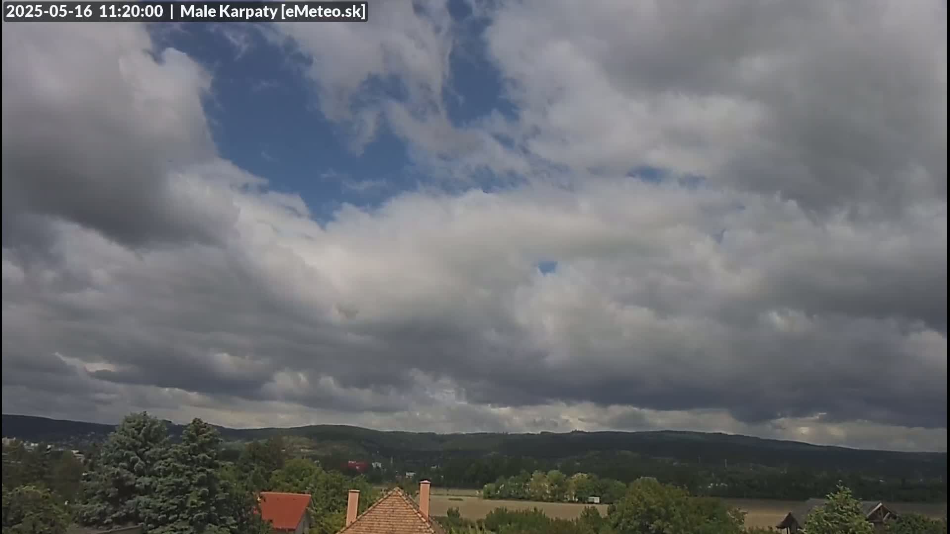 A partly cloudy sky hangs over a landscape of rolling green hills and houses with brown rooftops.