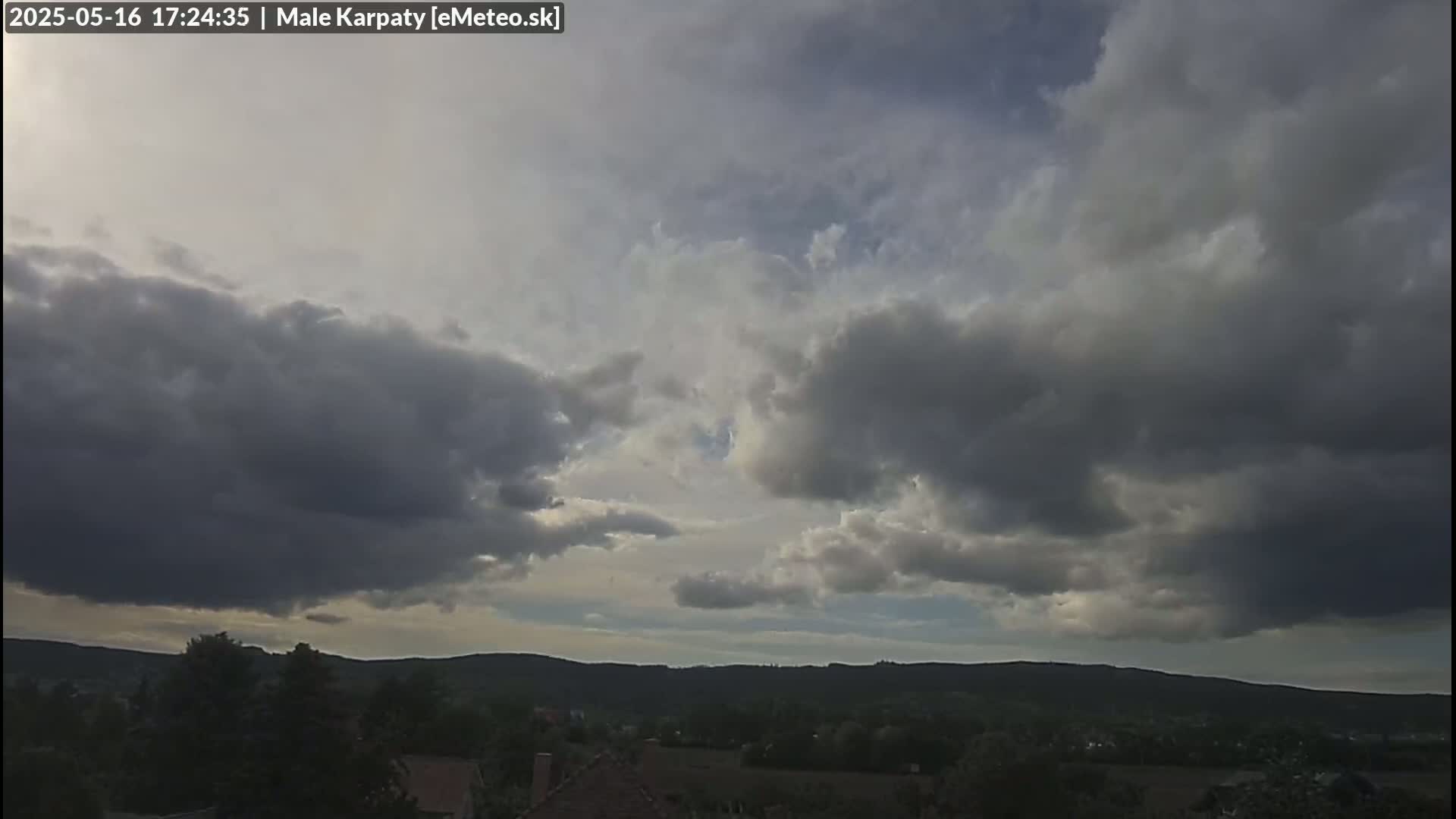 A mostly cloudy sky hangs over a landscape of rolling hills and trees.