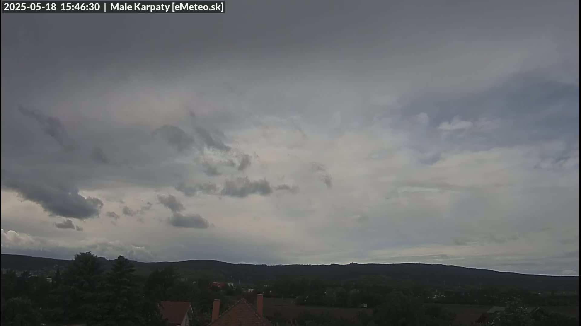 A mostly cloudy sky hangs over a landscape of dark green hills and a small village.