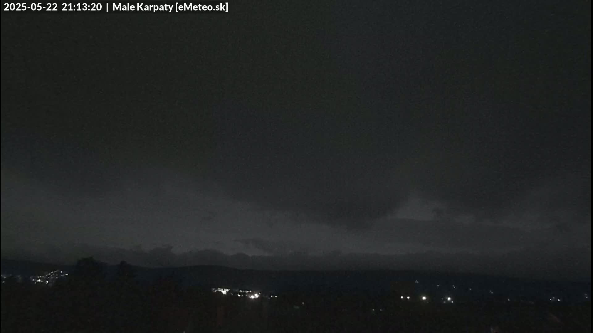 A nighttime view of dark, overcast skies above a dimly lit landscape of hills and distant lights.