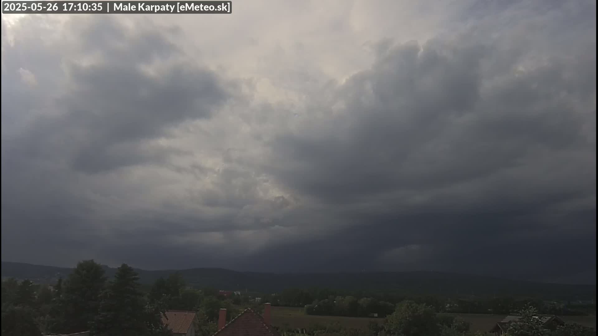 Dark, ominous clouds hang low over a landscape of green hills and houses, suggesting an impending storm.
