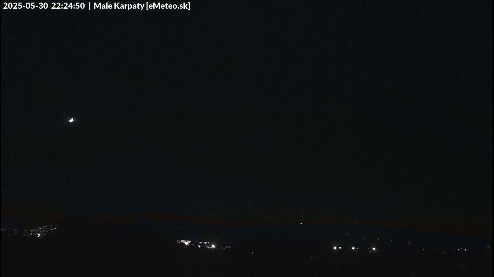 A crescent moon is visible in a dark night sky above a dimly lit landscape.