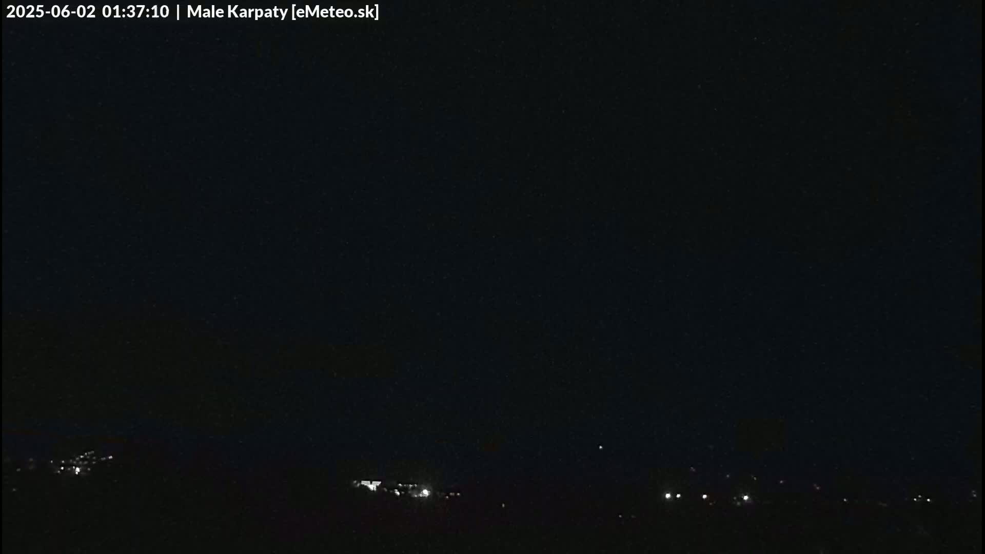 A dark nighttime scene shows a few faint lights on the horizon under a clear, black sky.