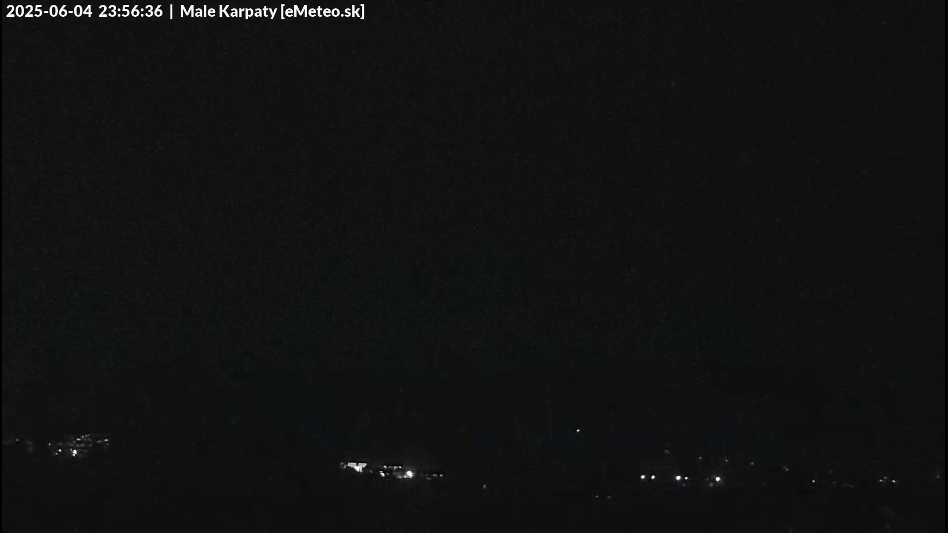 A nighttime, low-light outdoor image shows a dark sky and a barely visible line of lights at the bottom, possibly a town or village.