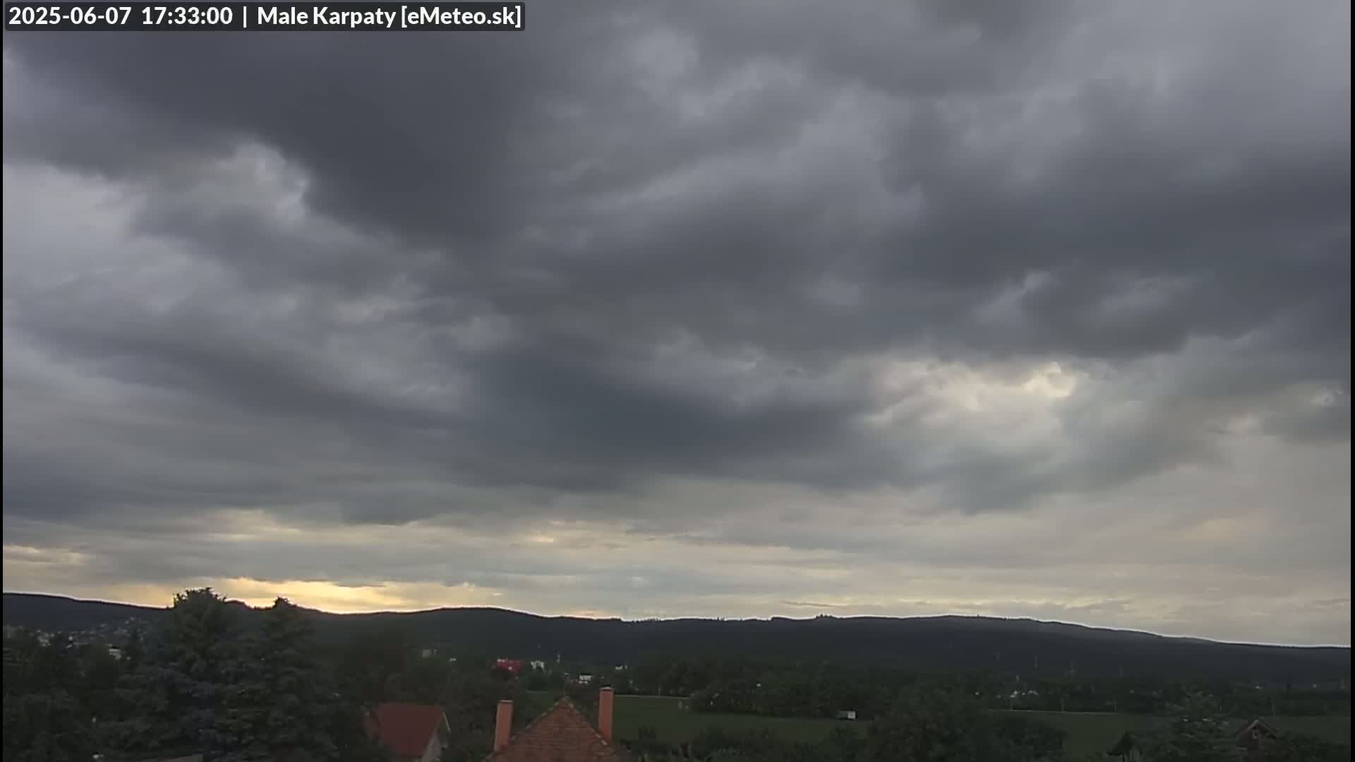 Overcast skies with dark gray clouds cover a landscape of rolling hills and trees.